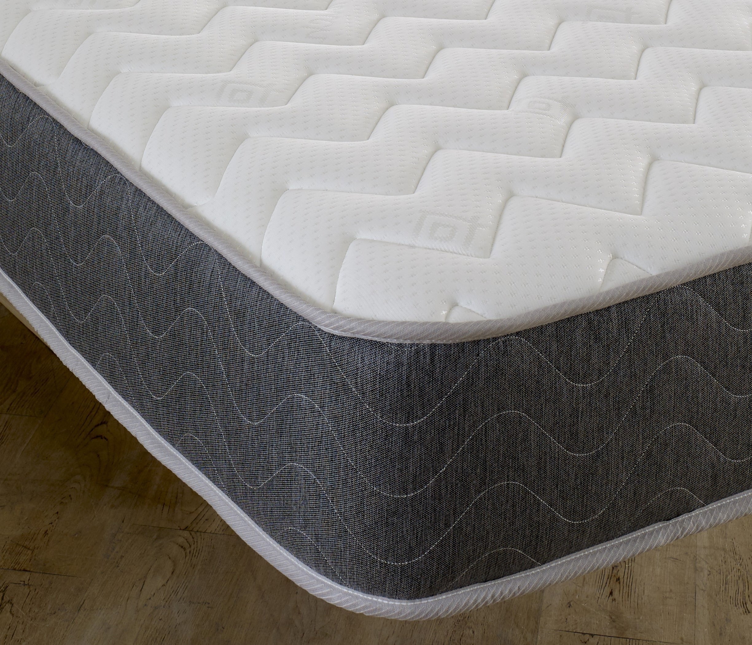 Close-up of mattress corner showing quilted white fabric top and dark grey fabric side with stitched pattern