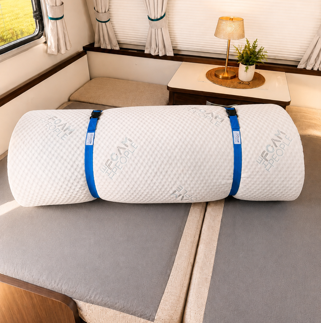 Rolled white foam mattress secured with two blue straps positioned on gray mattress foundation in camper van