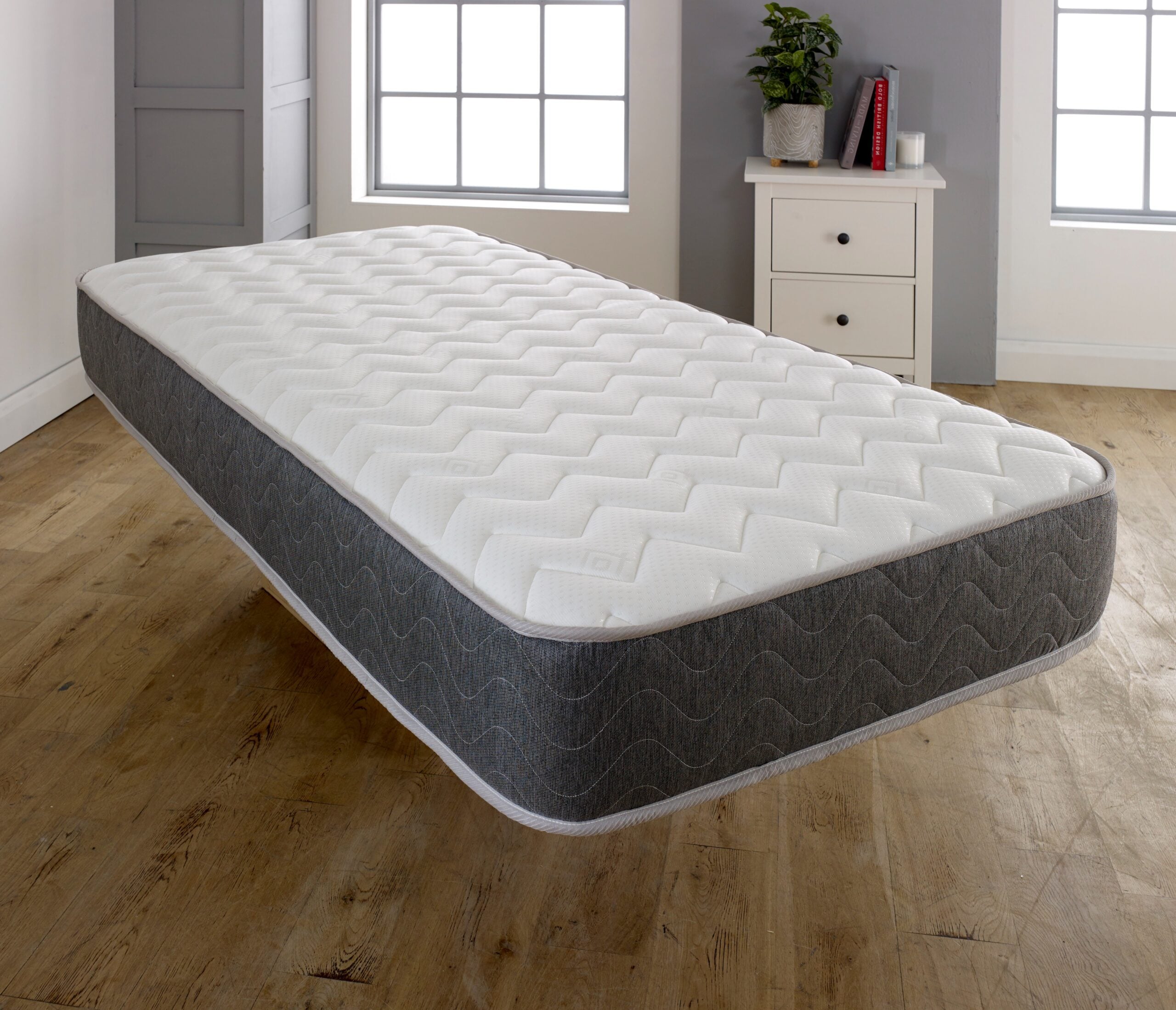 Single mattress viewed from above in bedroom showing white quilted surface and dark grey sides with piping
