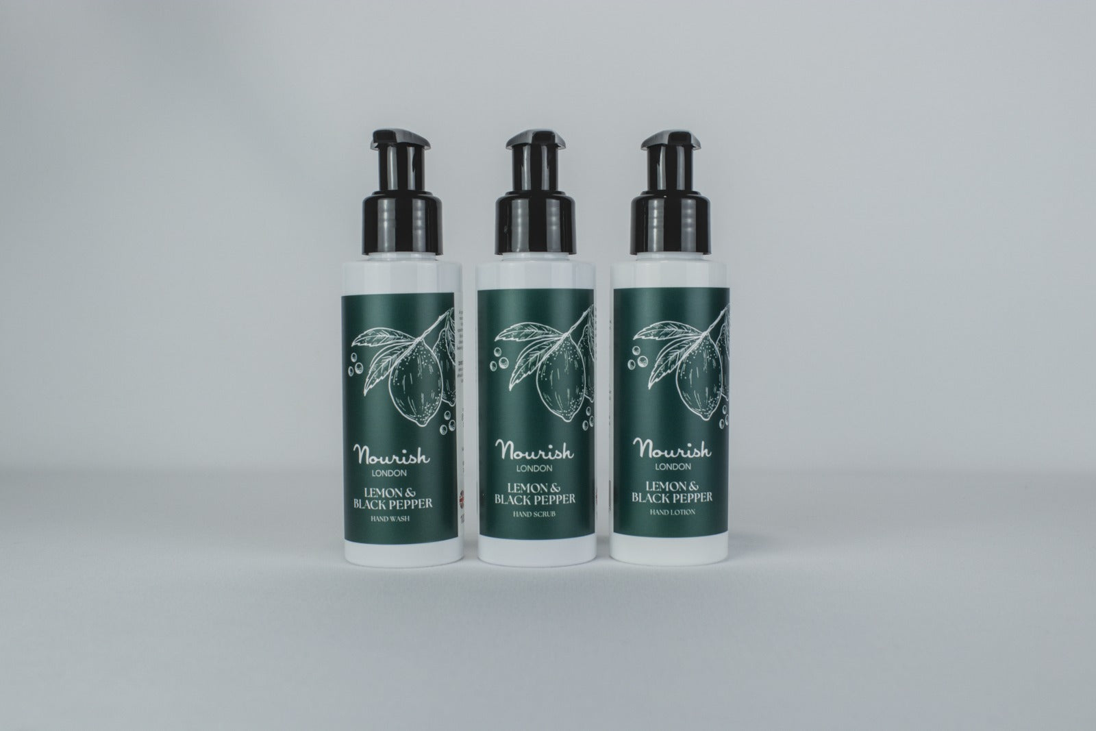 Three pump bottles with green labels and black caps arranged on light background showing hand care products